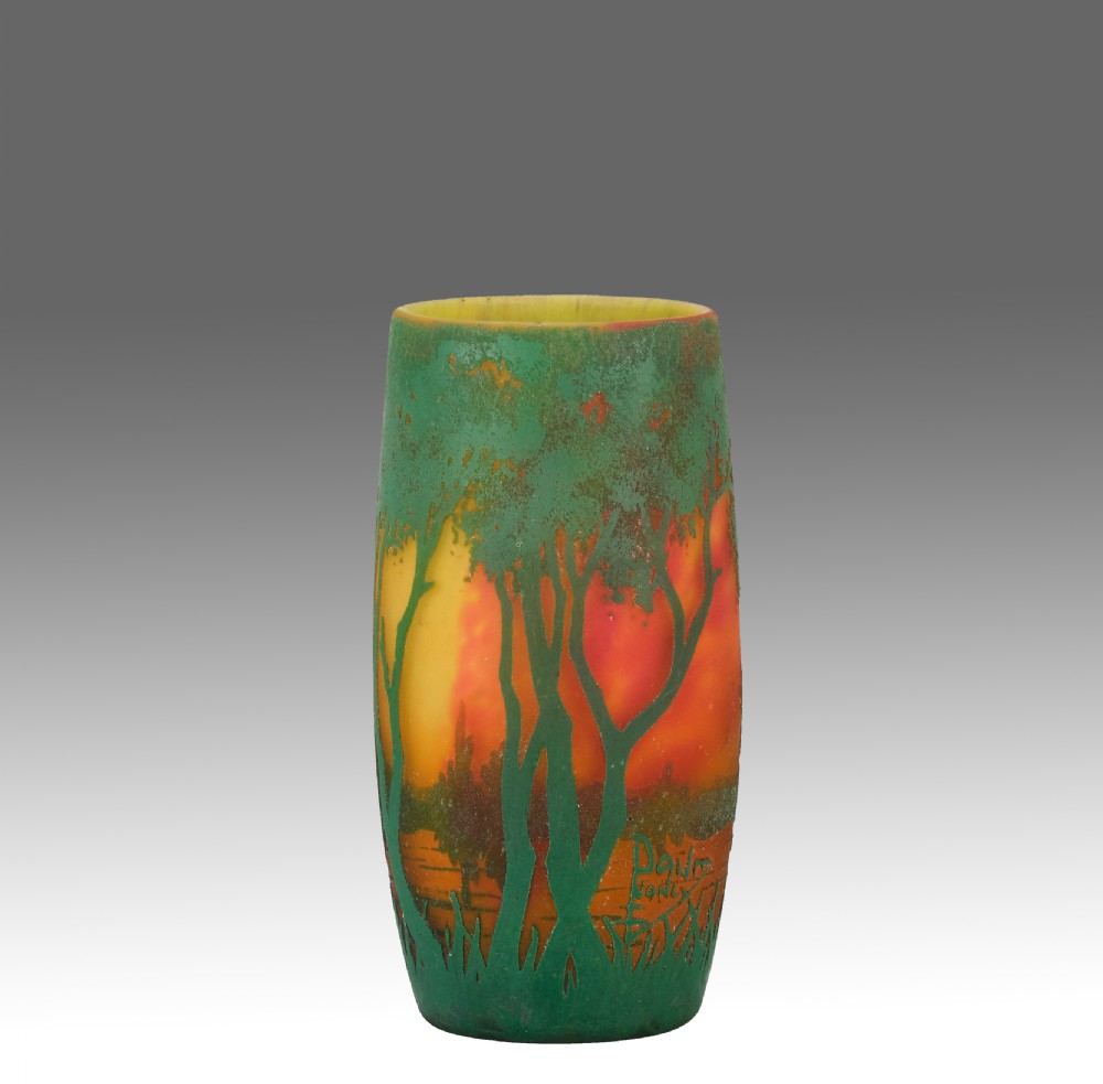An Art Nouveau frosted cameo glass vase featuring green etched tree silhouettes against a red, orange, and yellow sunset background.