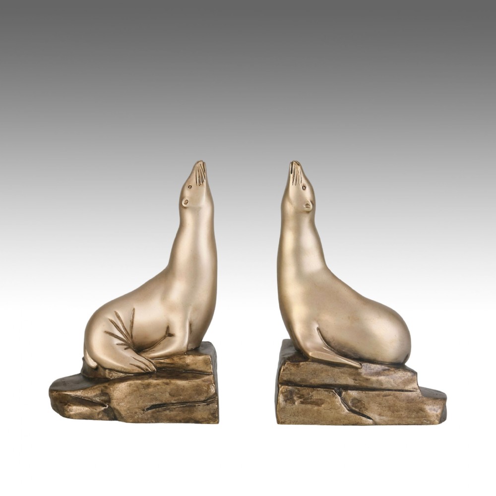 A pair of bronze Art Deco bookends shaped as sea lions resting on rocky bases with heads raised.
