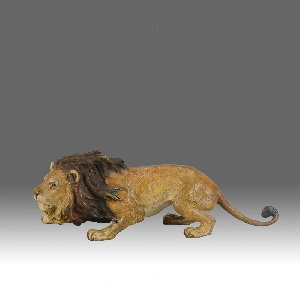 An early 20th-century cold-painted bronze figurine depicting a crouching lion with a dark brown mane and ochre coat.