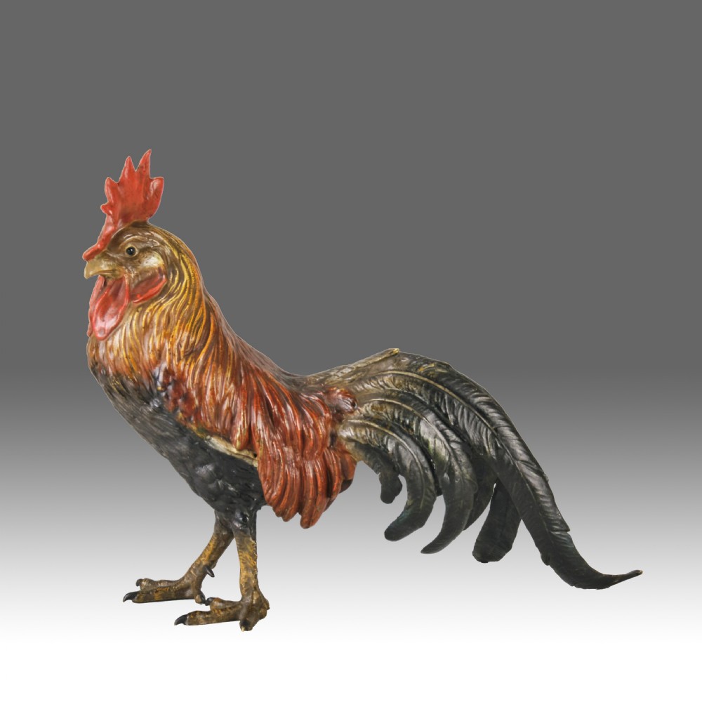 A cold-painted bronze figurine depicting a standing cockerel with a red comb and textured feathers in brown, ochre, and dark grey shades. View II