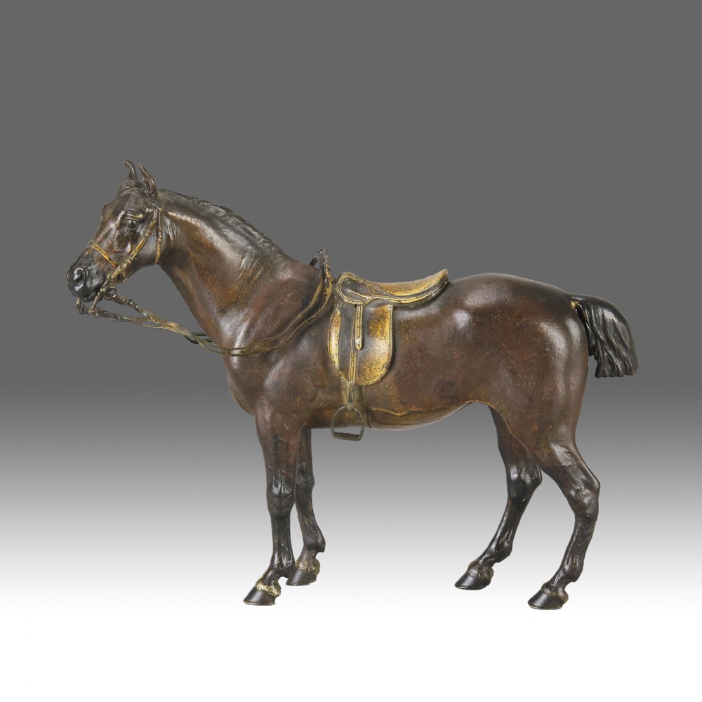 A cold-painted bronze sculpture depicting a saddled horse with gold-coloured tack, bridle, and stirrups in a standing pose.