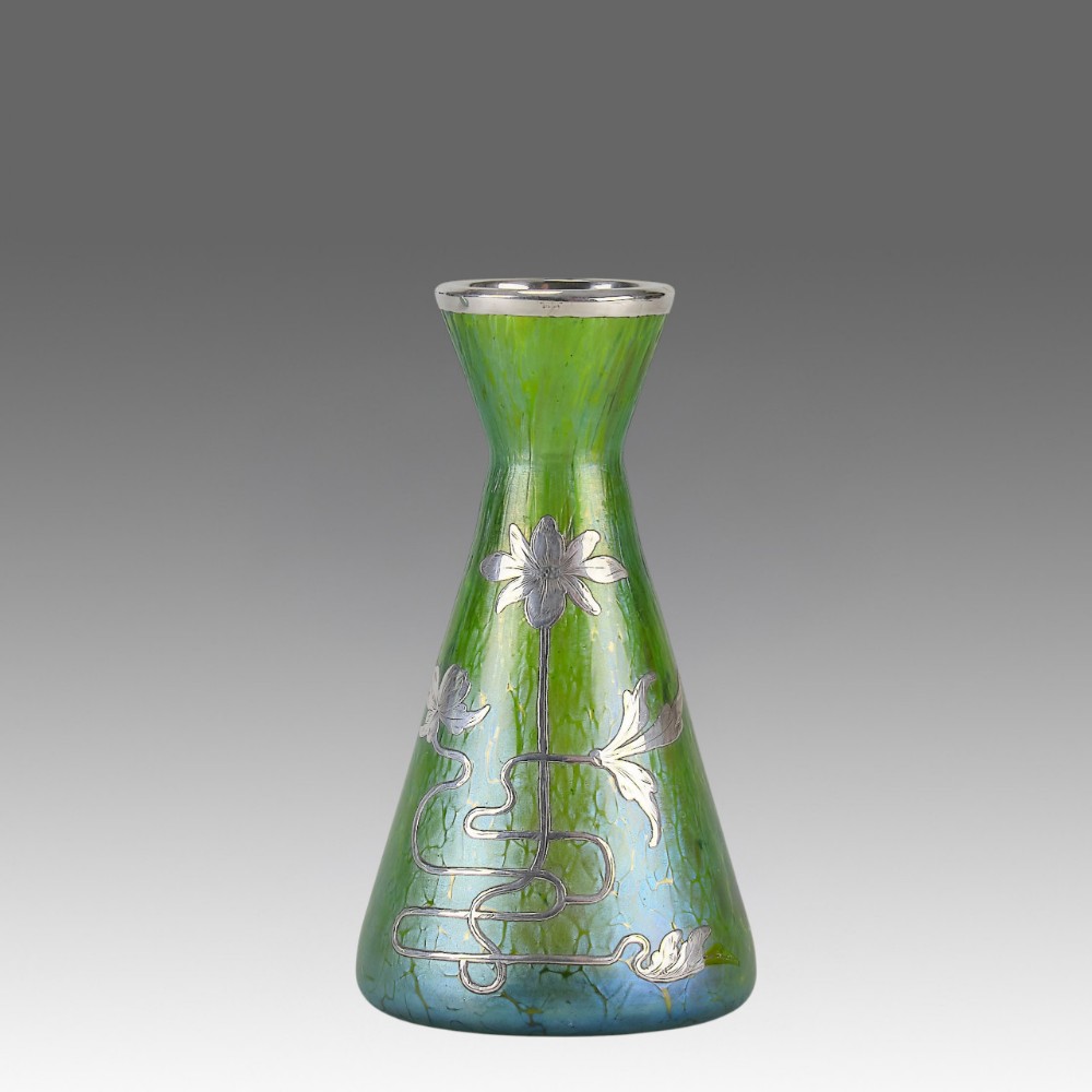 A conical iridescent green and blue glass vase decorated with an intricate silver overlay floral design and a silver rim.