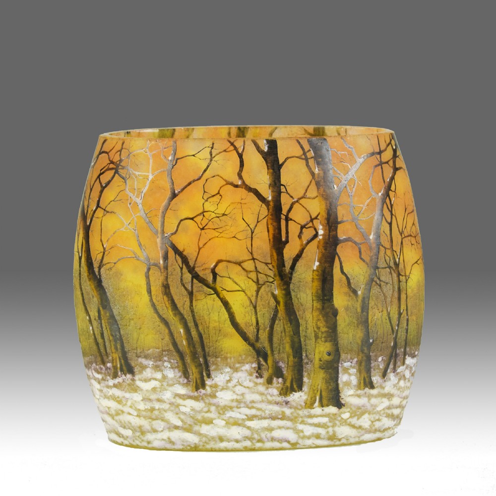 A barrel-shaped glass vase featuring an acid-etched and enamelled bare tree winter landscape scene over a yellow and orange background.