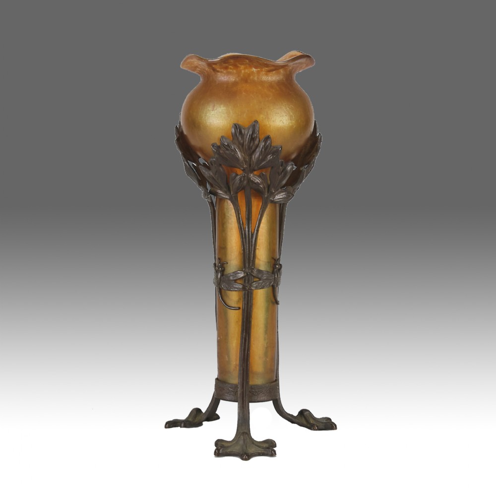 An Art Nouveau iridescent amber glass vase supported by a dark patinated bronze mount featuring sculpted leaves and dragonfly motifs on stylised tripod legs.