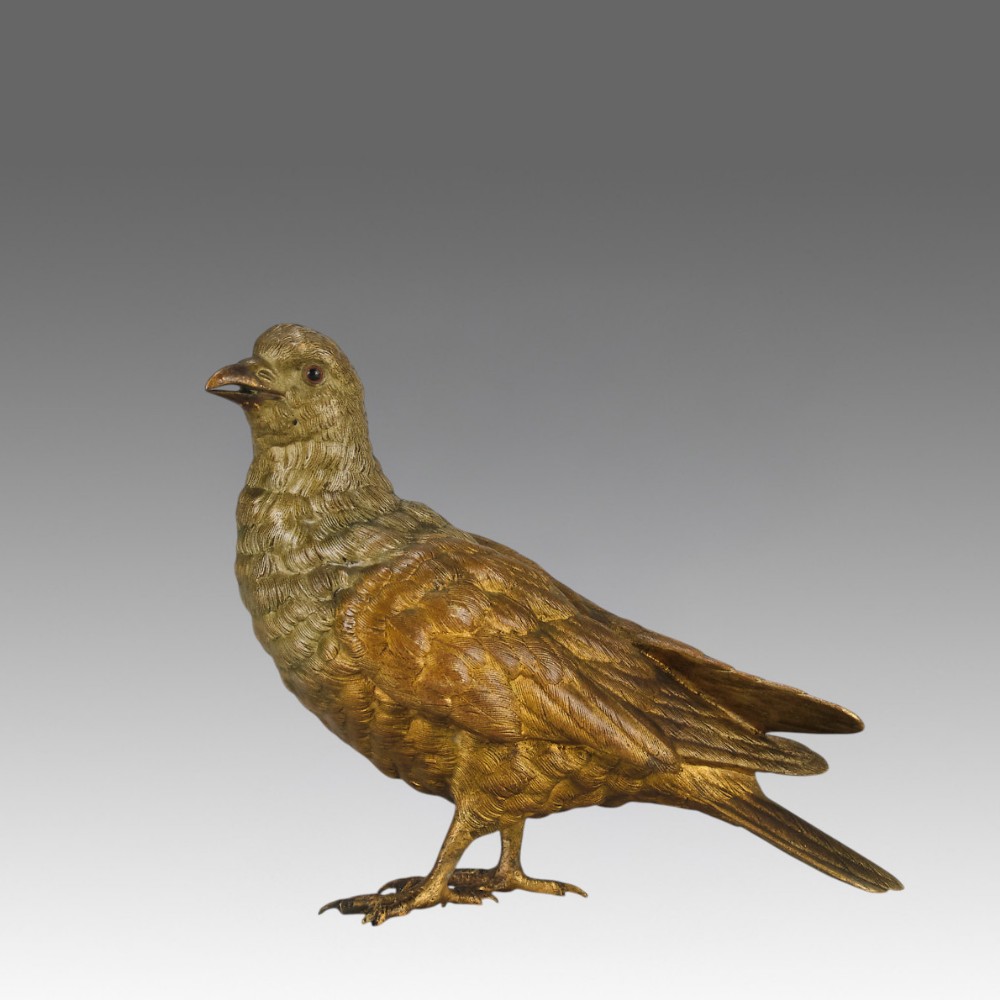 A cold-painted bronze figurine depicting a pigeon with textured feathers and a golden finish, standing facing left.