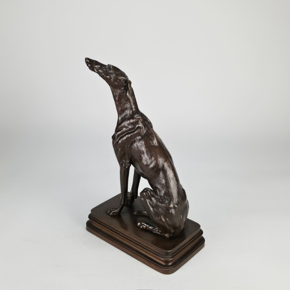 A late 19th-century dark brown patinated bronze sculpture depicting a seated greyhound with its head raised, resting on a rectangular stepped base. View IX