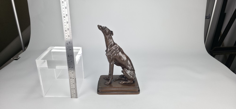 A late 19th-century dark brown patinated bronze sculpture depicting a seated greyhound with its head raised, resting on a rectangular stepped base. View XIII