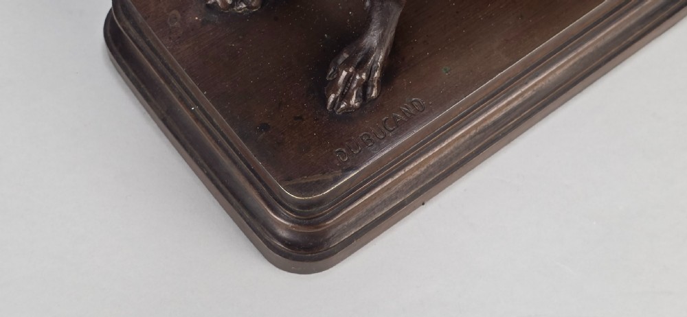 A late 19th-century dark brown patinated bronze sculpture depicting a seated greyhound with its head raised, resting on a rectangular stepped base. View XV