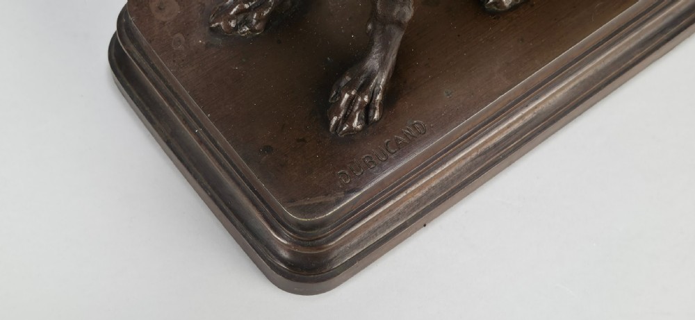 A late 19th-century dark brown patinated bronze sculpture depicting a seated greyhound with its head raised, resting on a rectangular stepped base. View XVI