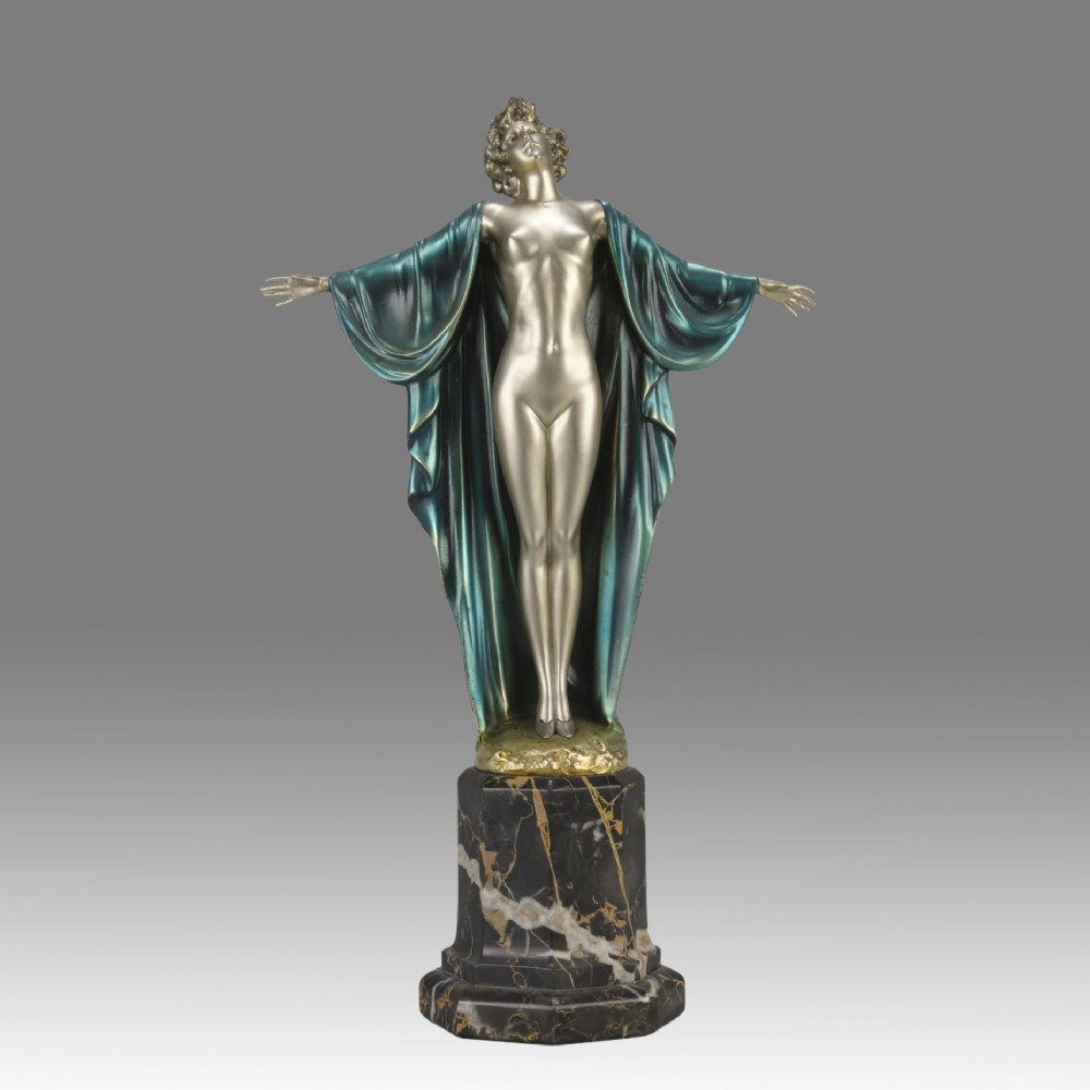 An Art Deco cold-painted bronze sculpture depicting a silver female figure with outstretched arms wearing a teal cape, mounted on a black veined marble pedestal.