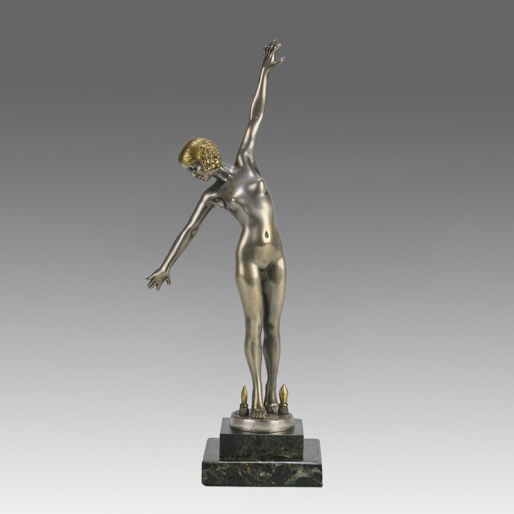 An Art Deco silver-toned cold-painted bronze sculpture depicting a standing female dancer raised on a dark green marble pedestal base.