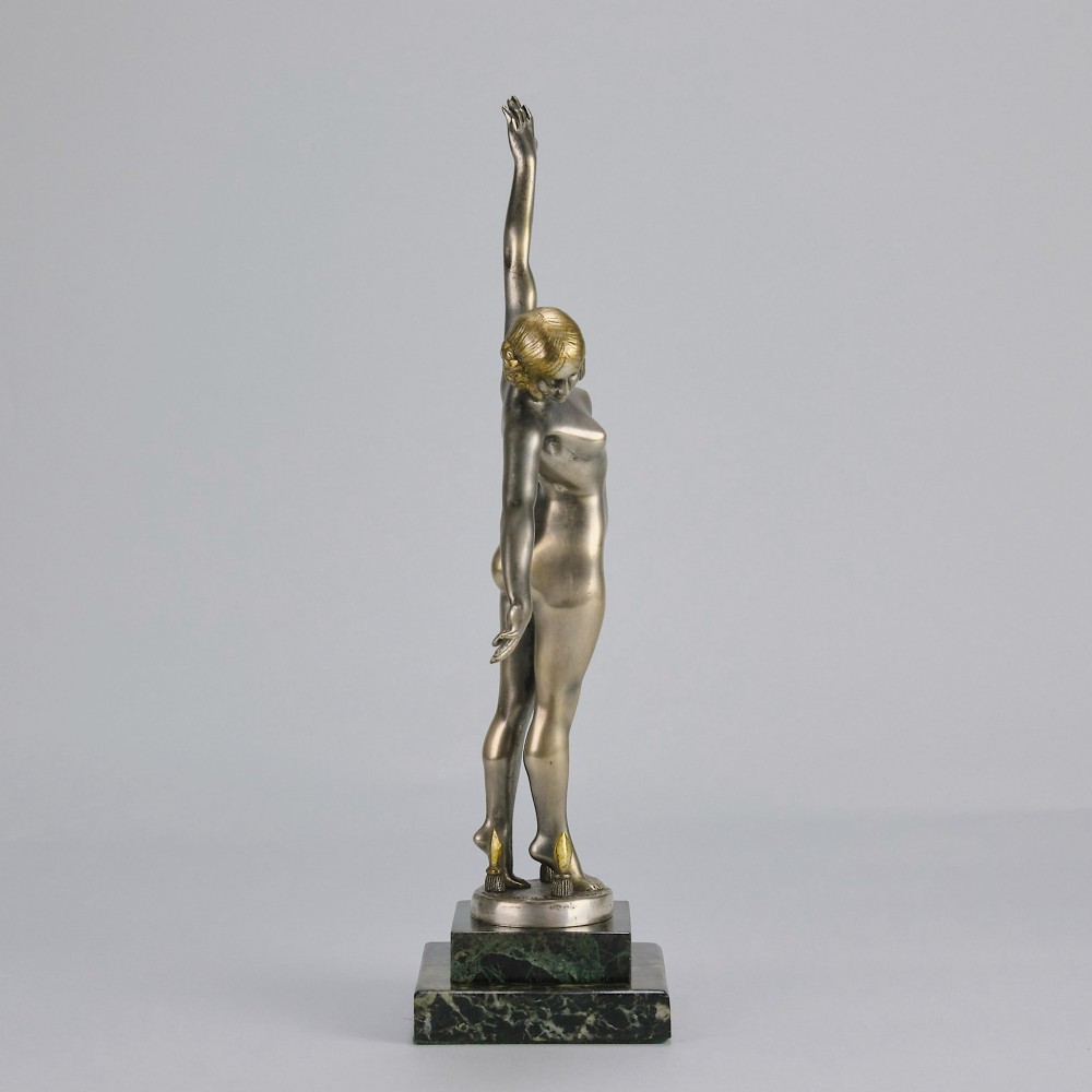 An Art Deco silver-toned cold-painted bronze sculpture depicting a standing female dancer raised on a dark green marble pedestal base. View IV