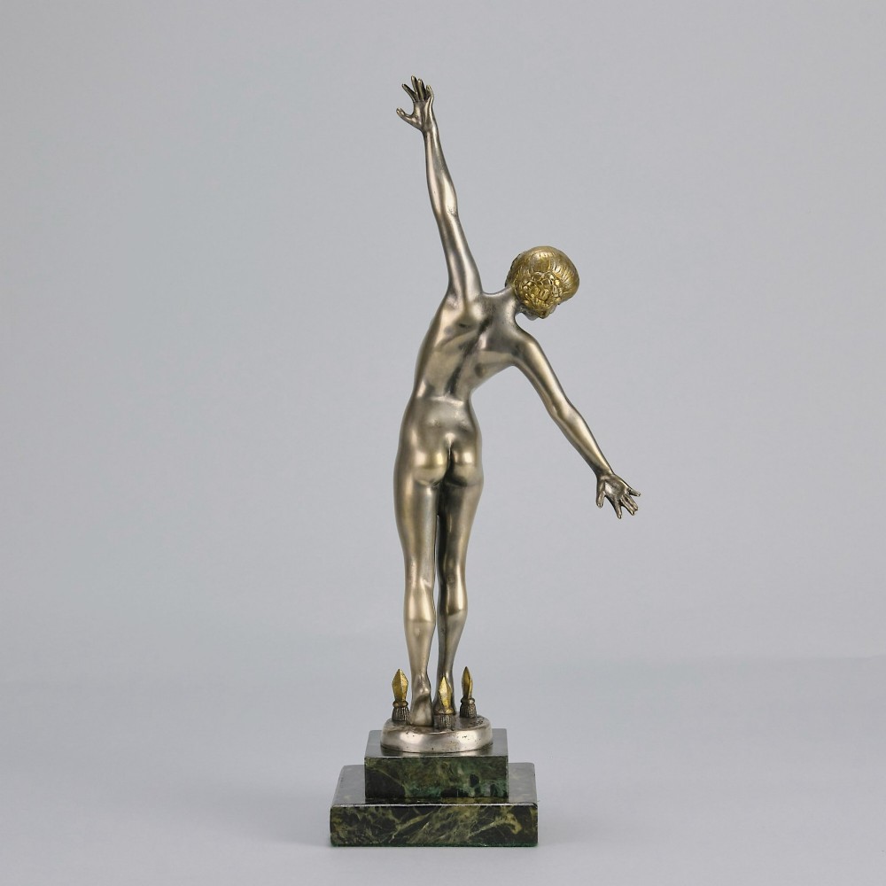 An Art Deco silver-toned cold-painted bronze sculpture depicting a standing female dancer raised on a dark green marble pedestal base. View VI
