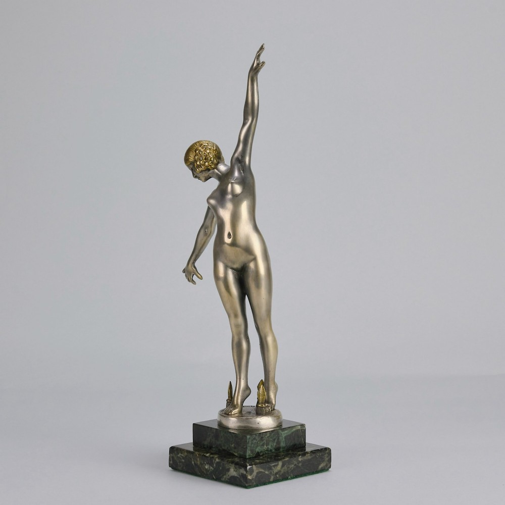 An Art Deco silver-toned cold-painted bronze sculpture depicting a standing female dancer raised on a dark green marble pedestal base. View VIII