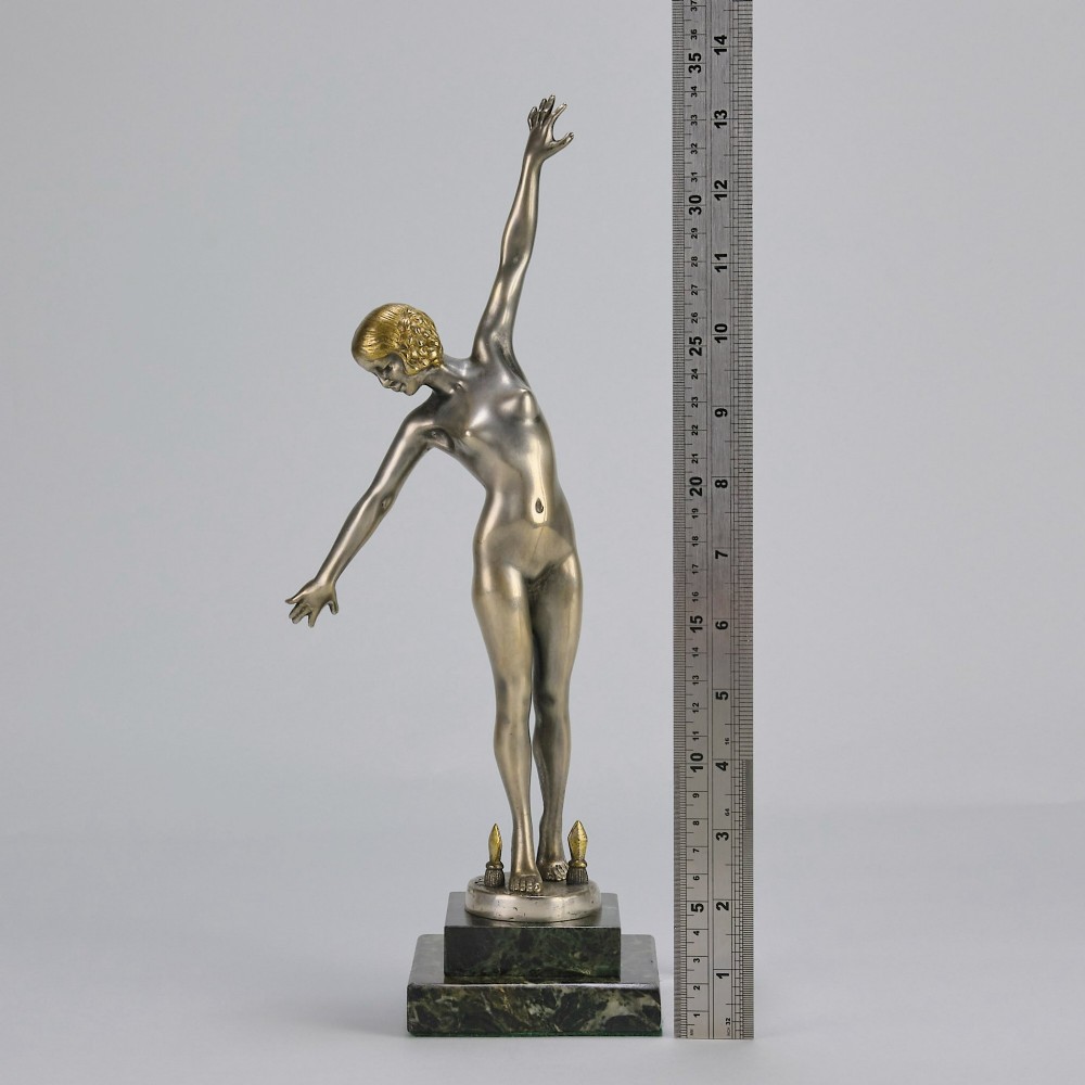 An Art Deco silver-toned cold-painted bronze sculpture depicting a standing female dancer raised on a dark green marble pedestal base. View IX