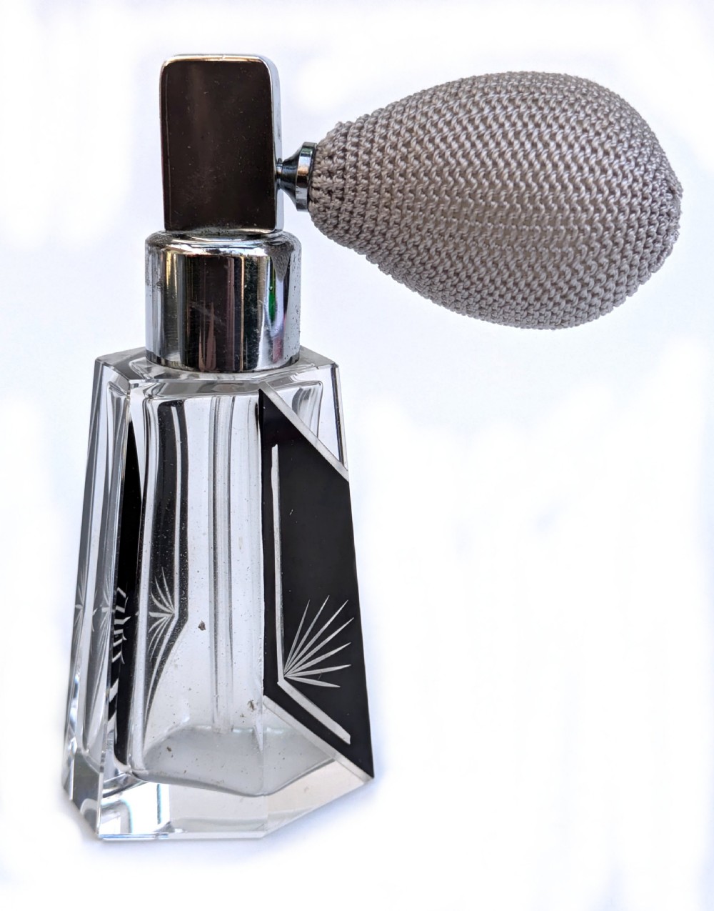 A geometric clear glass Art Deco perfume atomiser bottle featuring black enamel panels, etched sunburst motifs, a chrome spray nozzle, and a grey woven fabric bulb. View VI