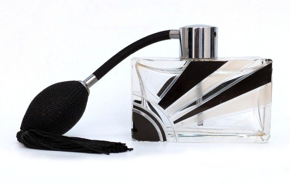 An Art Deco rectangular cut glass perfume atomiser featuring a black enamelled sunray pattern and a chrome top connected to a black fabric bulb with a tassel.