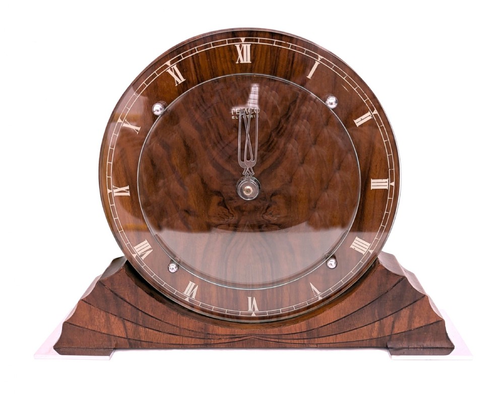 An Art Deco circular walnut mantel clock featuring inlaid Roman numerals and a stepped contoured base.