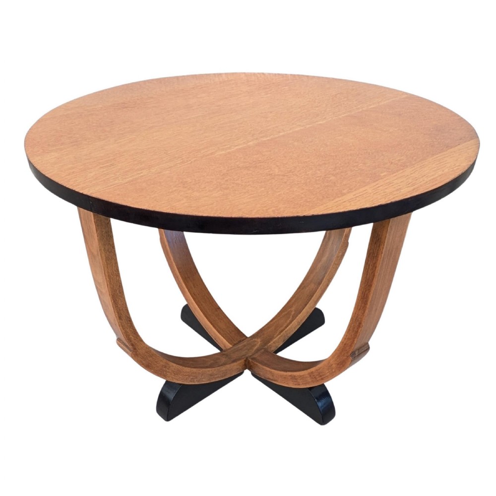 A round Art Deco blonde oak coffee table featuring sweeping curved legs and contrasting ebonised rim and cross base.