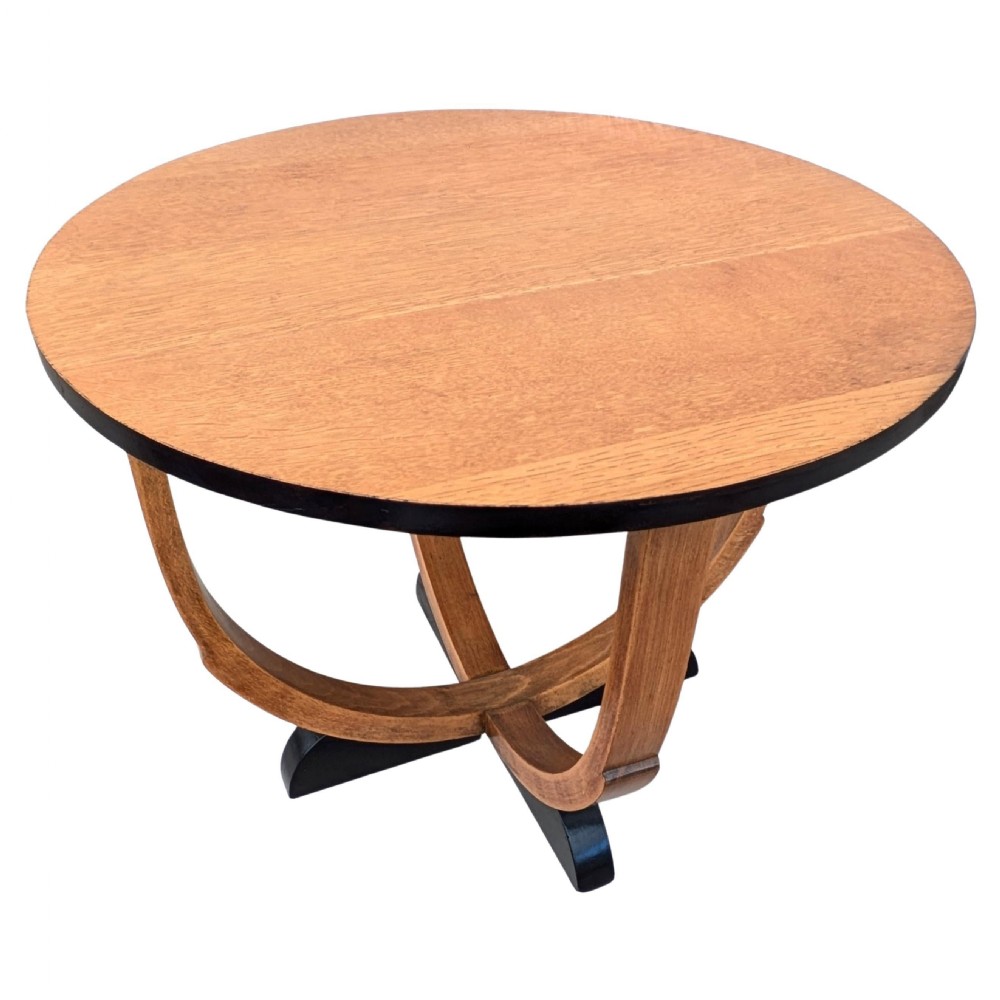 A round Art Deco blonde oak coffee table featuring sweeping curved legs and contrasting ebonised rim and cross base. View X