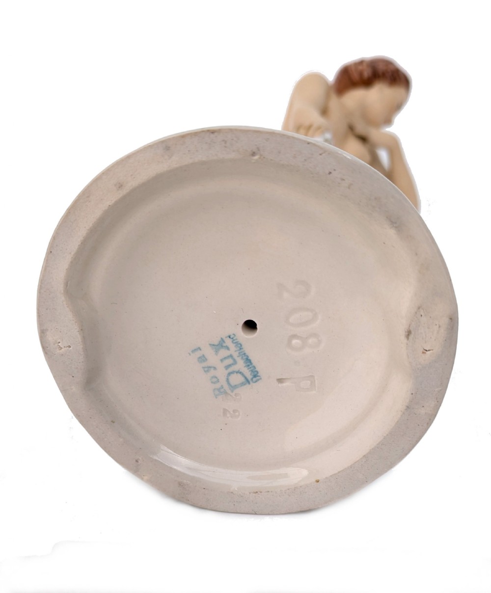 An Art Deco glazed porcelain figurine depicting a standing nude female figure holding a soft pink patterned drape on a rounded cream base. View IX