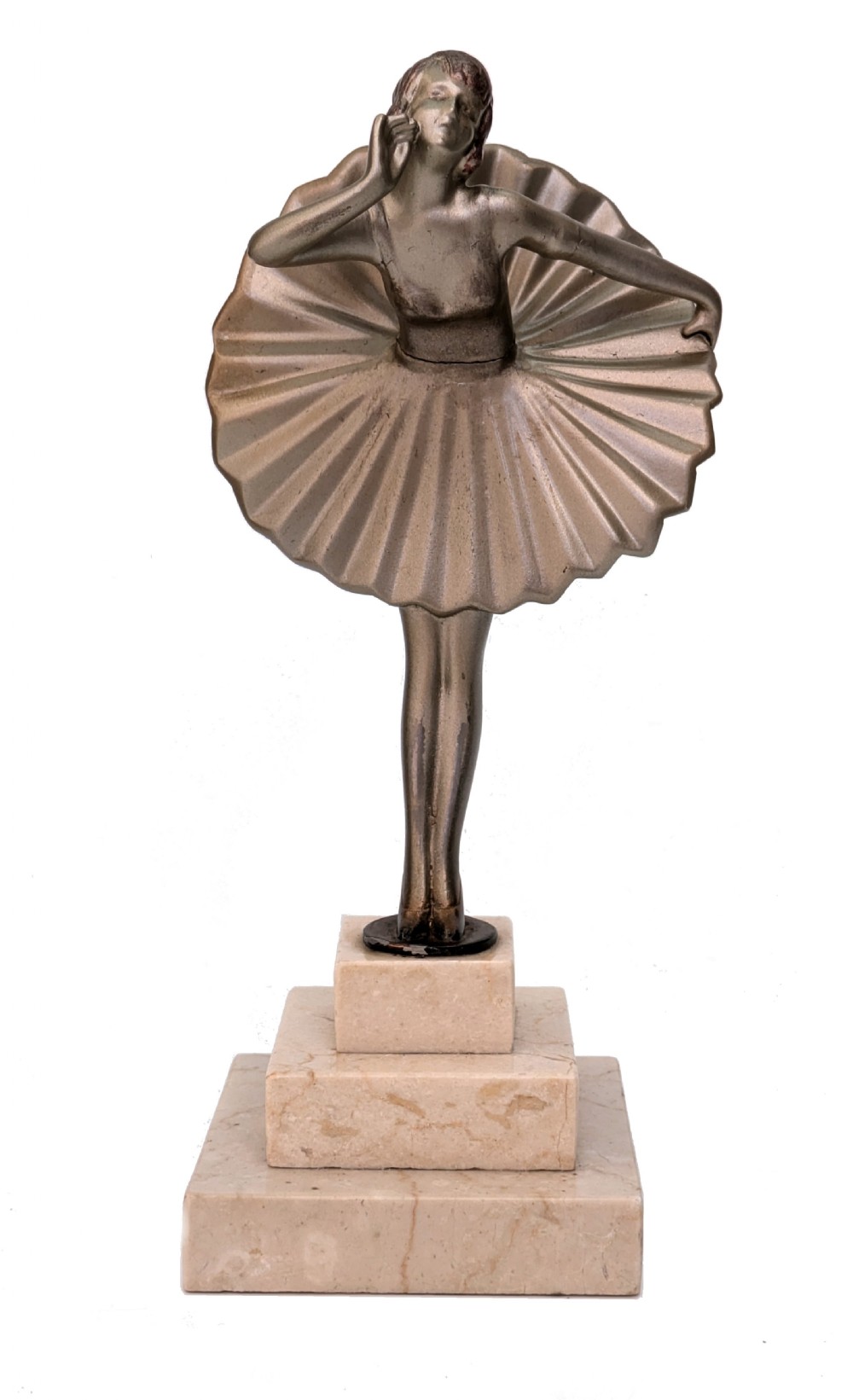 An Art Deco spelter sculpture depicting a female dancer in a stylized fan dress, standing on a three-tiered beige marble plinth.