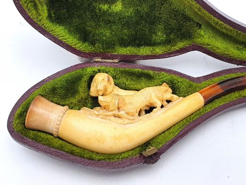 fig 1. An antique carved meerschaum cheroot holder featuring detailed hunting dogs resting inside a green velvet-lined fitted case.