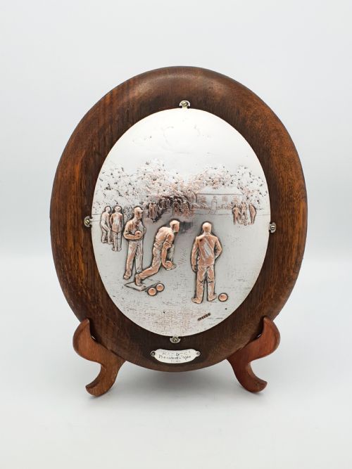 fig 1. An oval timber plaque displaying an embossed silver-plated metal relief depiction of late Victorian lawn bowling players dated 1899.