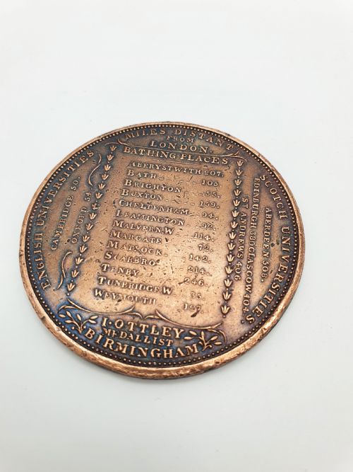 fig 1. A circular patinated bronze medallion featuring radiating text detailing distances in miles from London to various British towns and cities.