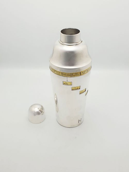 fig 1. A vintage silver-plated cocktail shaker featuring a rotating outer body with cutout windows displaying drink ingredient recipes.