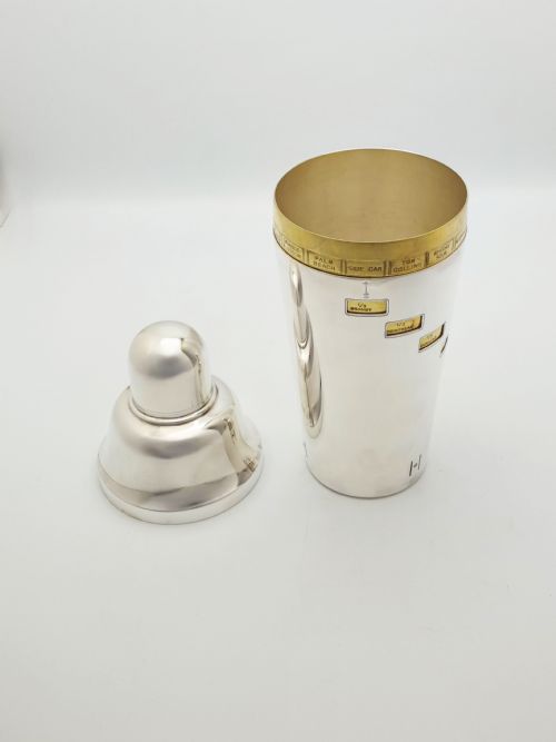 fig 2. A vintage silver-plated cocktail shaker featuring a rotating outer body with cutout windows displaying drink ingredient recipes.