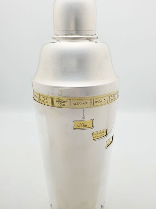 fig 4. A vintage silver-plated cocktail shaker featuring a rotating outer body with cutout windows displaying drink ingredient recipes.