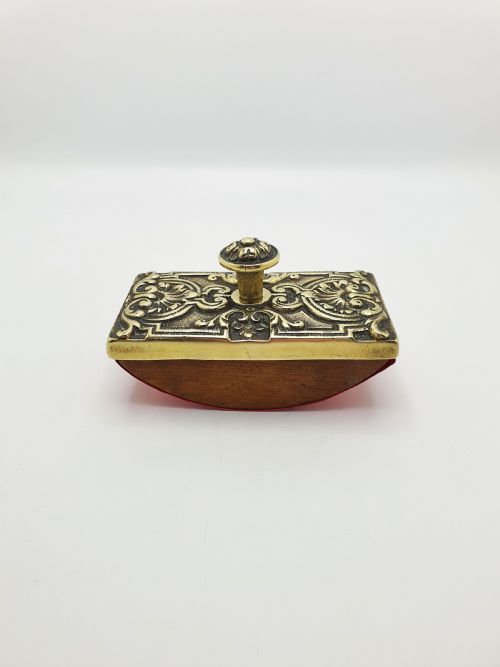 fig 1. An Edwardian brass and wood rocker ink blotter featuring an ornate cast brass top plate decorated with relief scrollwork and a central turned brass knob handle.