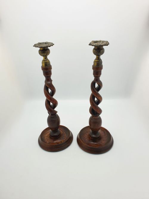 fig 1. A pair of dark oak candlesticks featuring open barley twist shafts, circular stepped bases, and metal brass sconces.