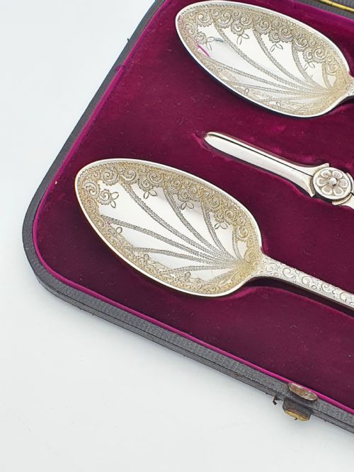 fig 1. An open black presentation box lined with magenta velvet containing two engraved silver serving spoons and matching grape shears.