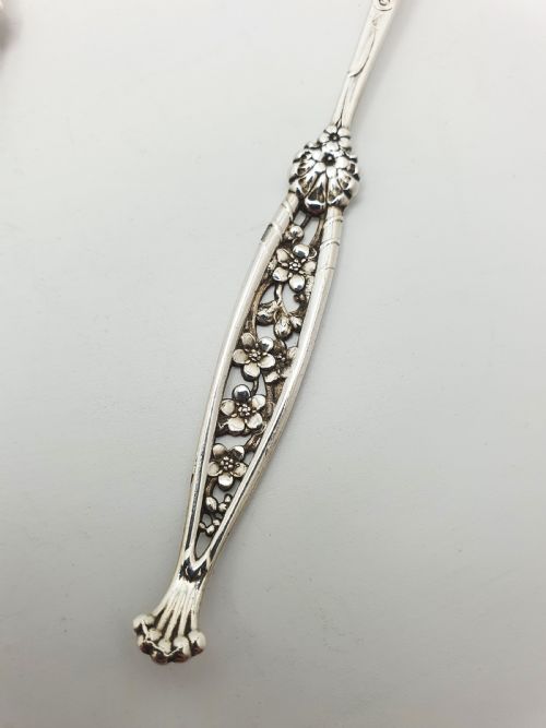 fig 2. A set of twelve sterling silver seafood forks with ornate floral handles and gold gilt tines arranged in a diagonal line.