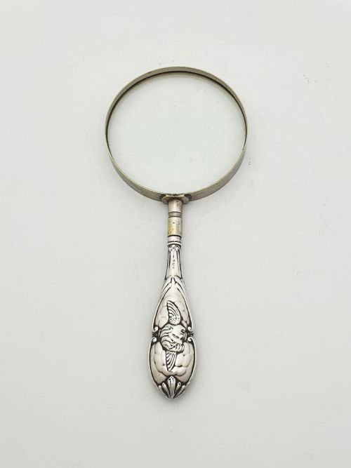 fig 1. An Edwardian magnifying glass featuring a circular glass lens in a metal rim attached to an embossed sterling silver handle.