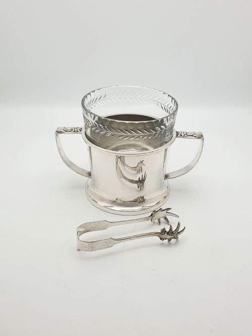 fig 1. An Art Deco silver-plated ice bucket featuring twin handles, a removable cut-glass liner with a leaf pattern, and matching ice tongs.