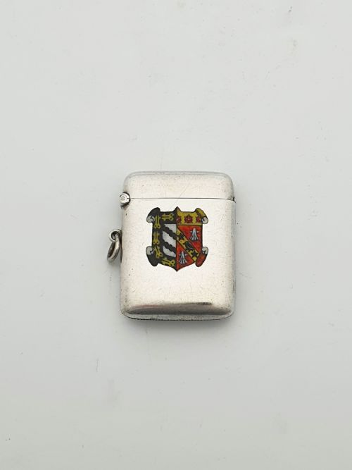 fig 1. A rectangular sterling silver vesta case featuring a hinged top, side suspension ring, bottom striker, and a colourful heraldic enamel crest on the front.