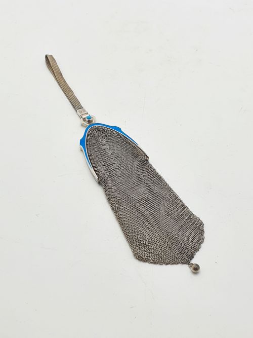 fig 2. An antique silver mesh purse featuring a blue guilloche enamel top frame, a woven silver strap, and a hanging metal drop.