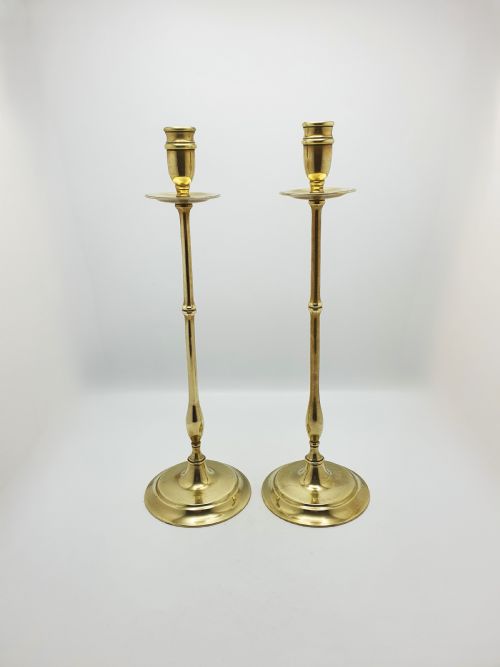 fig 1. A pair of tall antique Edwardian brass candlesticks featuring slender turned stems, wide drip pans, and circular stepped bases.