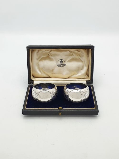 fig 1. A pair of engraved sterling silver napkin rings with circular cartouches resting inside a dark blue velvet-lined presentation box.