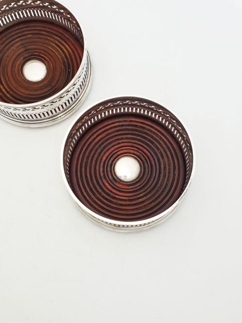 fig 1. A pair of circular silver plated wine coasters featuring pierced fretwork sides, turned mahogany bases with central silver bosses, and dark felt underneath.