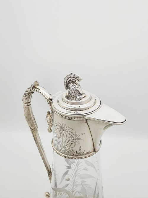 fig 1. A Victorian etched clear glass claret jug featuring botanical engravings and a silver-plated handle, spout, and helmet finial.