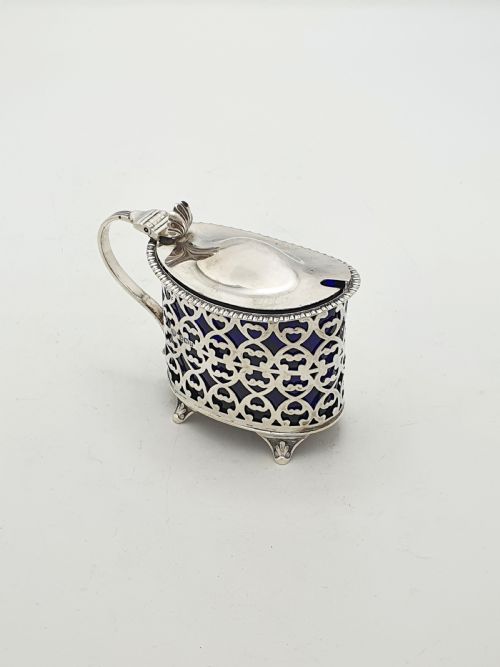 fig 1. A Victorian sterling silver mustard pot with openwork lattice piercing, a hinged lid, a scroll handle, and a removable cobalt blue glass liner.