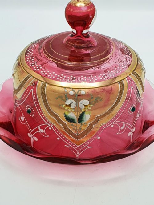 fig 1. An antique cranberry red glass covered cheese dish featuring gold filigree detailing, floral enamel panels, and a rounded glass knob finial.