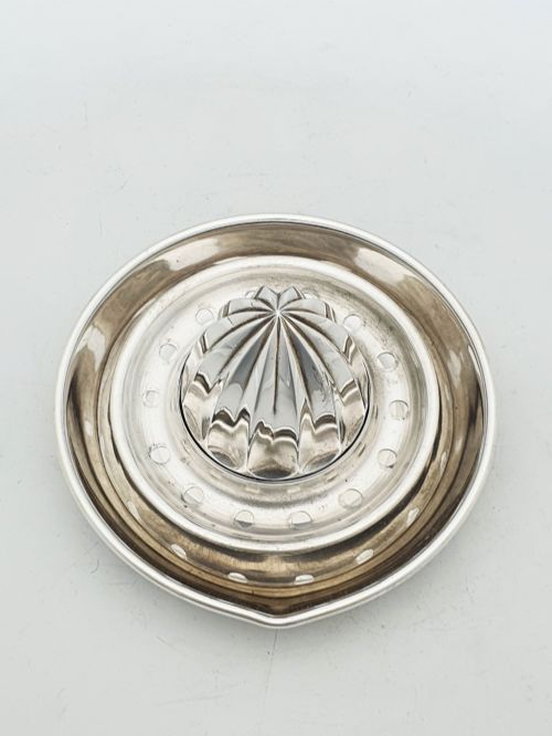 fig 1. A silver-plated manual citrus squeezer featuring a central fluted reamer cone, a circular perforated strainer ring, and a shallow catch tray.