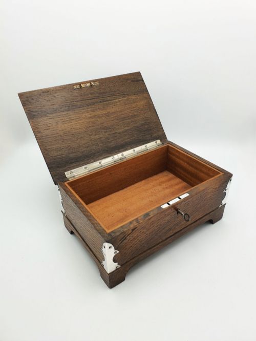 fig 1. An Edwardian oak cigar box featuring decorative sterling silver corner mounts, a central shaped silver plaque, and a front keyhole with key.