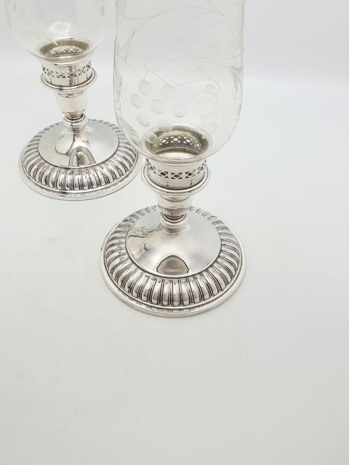 fig 2. A pair of silver-plated candlestick bases fitted with clear etched glass hurricane shades featuring subtle floral patterns.