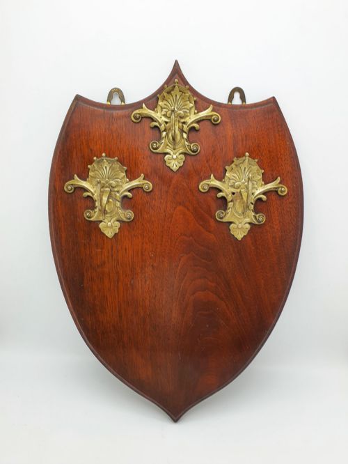 fig 1. A shield-shaped mahogany wall plaque equipped with three decorative cast brass coat hooks arranged symmetrically.